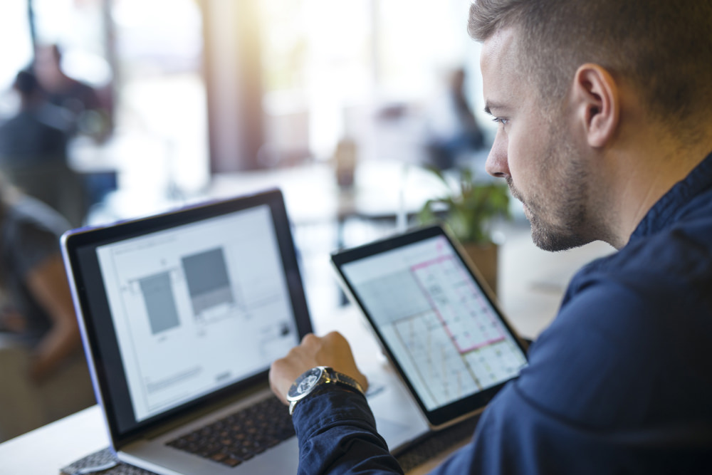 A man looking over data reports on a laptop and iPad